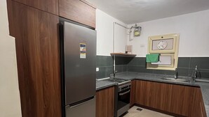 A kitchen with wooden cabinets, a stainless steel refrigerator, a gas stove, and a built-in oven. - Spacious 3-bedroom apartment in the heart of Sheikh Zayed with Garden view (Giza Governorate)