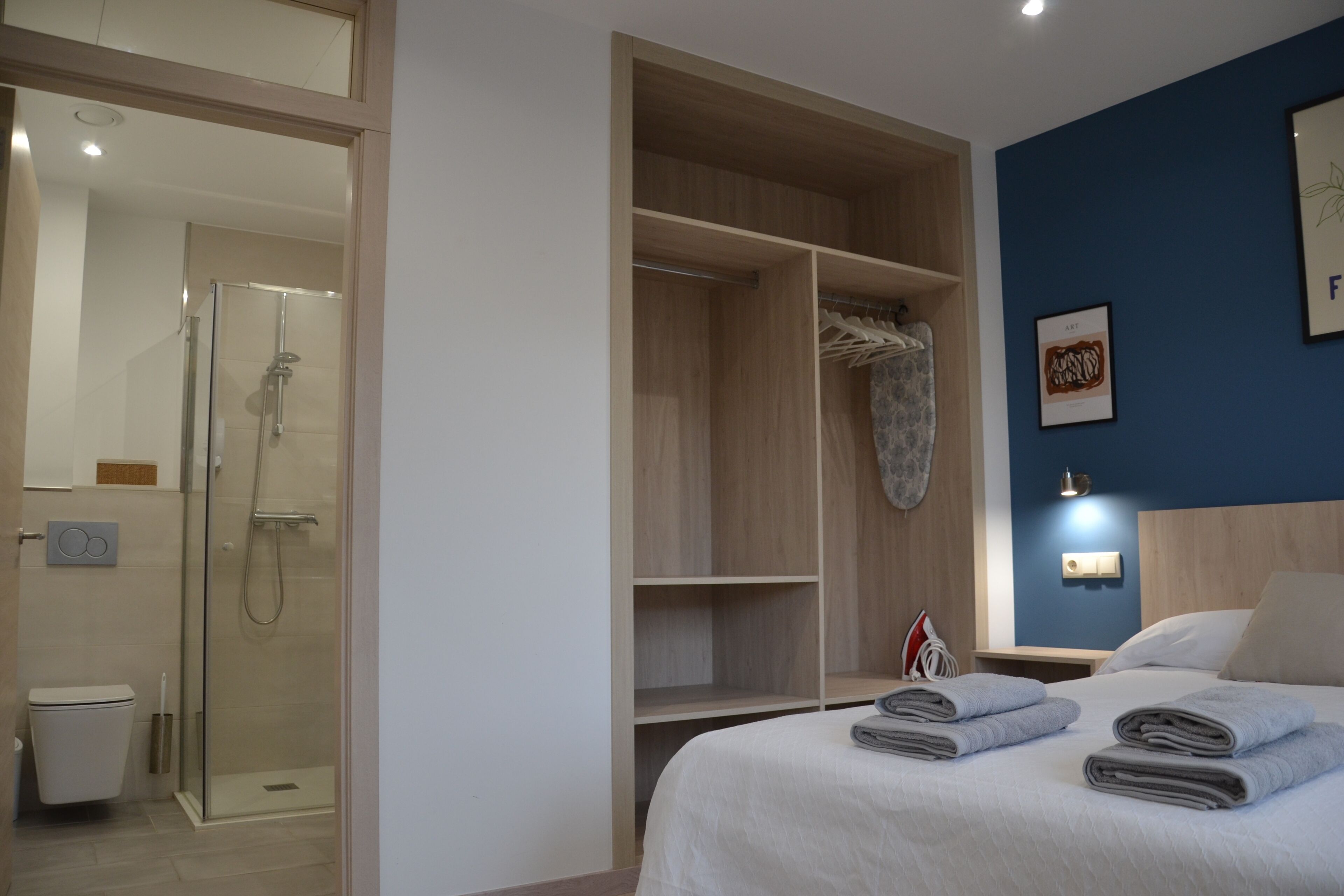 Una habitación de hotel con cama, vestidor, ducha y luz empotrada.