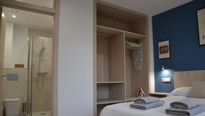 Una habitación de hotel con cama, vestidor, ducha y luz empotrada.