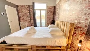 Quarto com estrutura de cama de madeira, radiador, luminária e parede de tijolos.