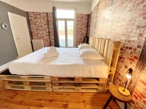 Une chambre avec un lit en bois, un radiateur, une lampe et un mur en briques.