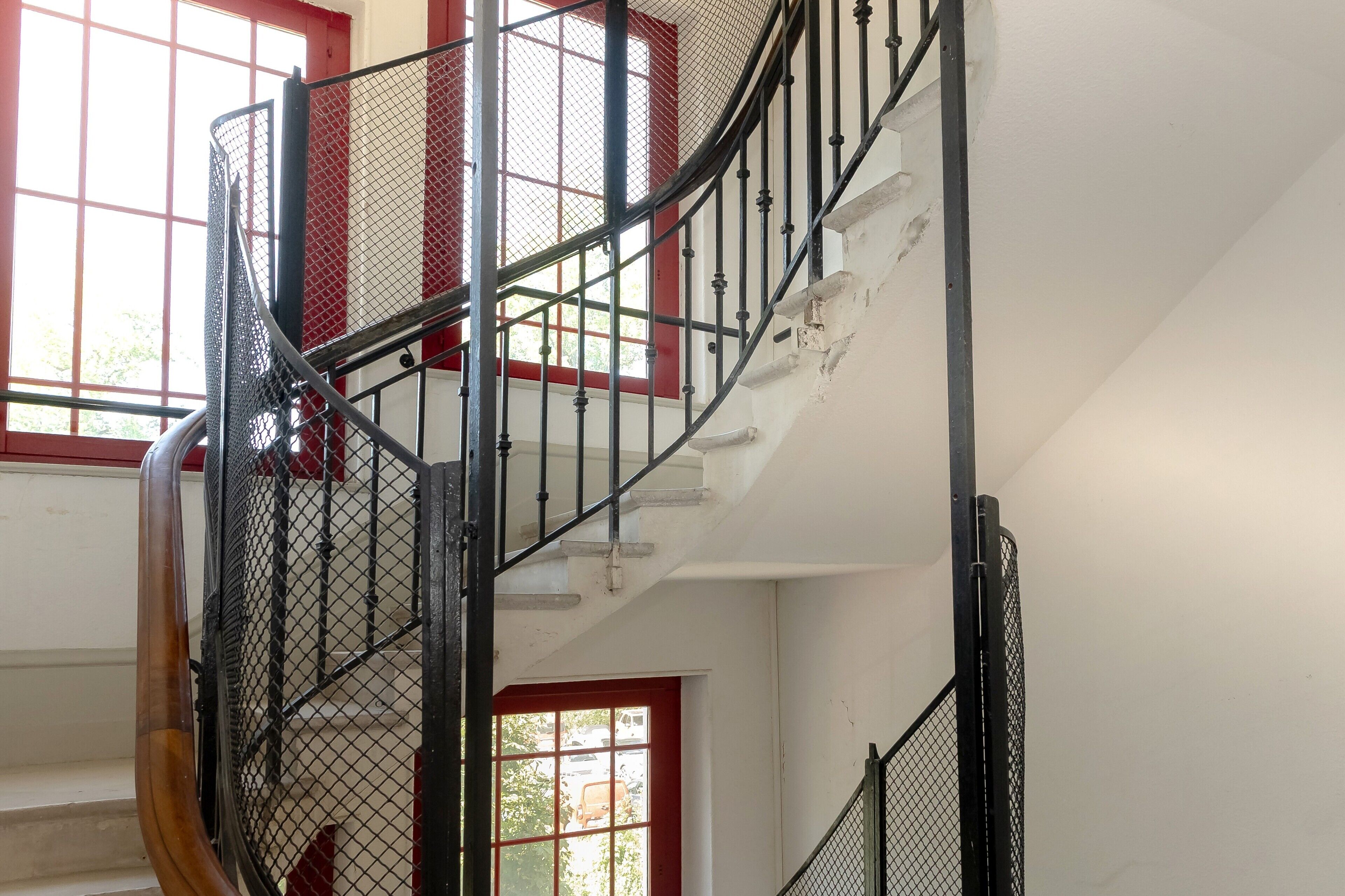 A spiral staircase with metal railings and a red door at the bottom.