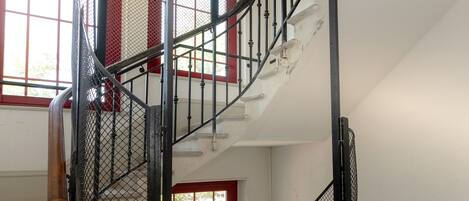 Un escalier en colimaçon avec des rampes en métal et une porte rouge en bas.