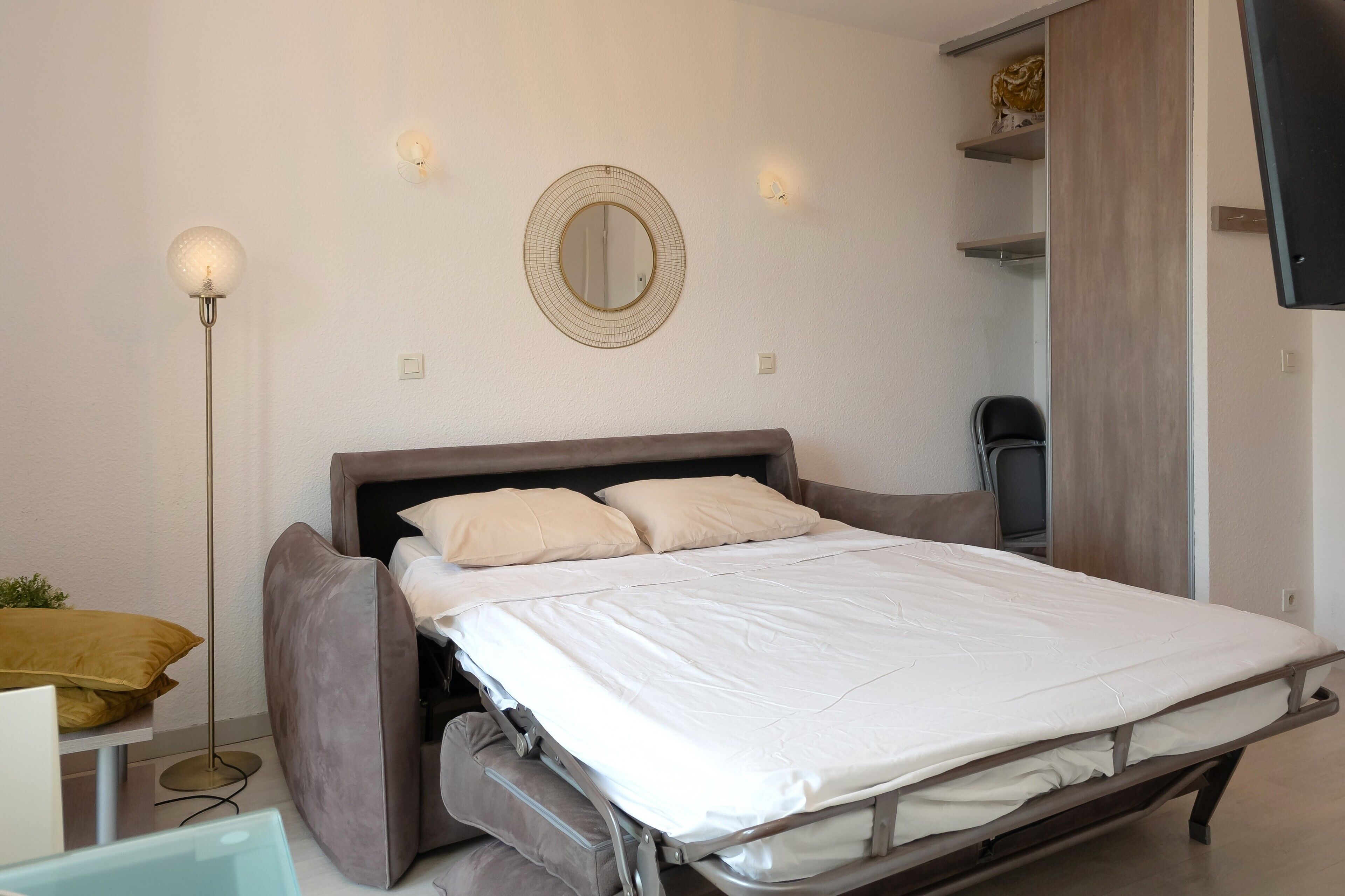 A modern bedroom with a bed, bedside table, floor lamp, and a mirror on the wall.