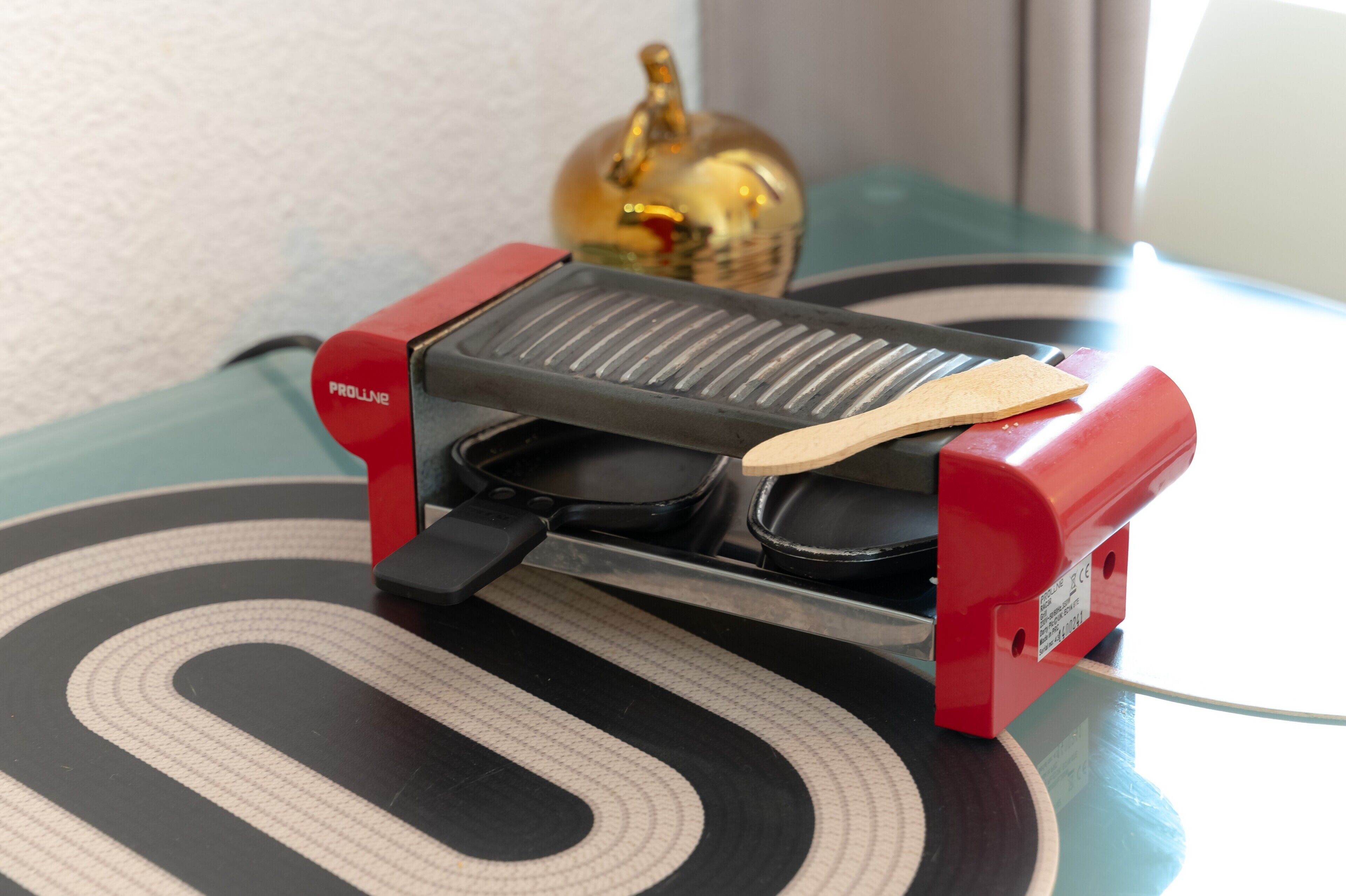 A waffle maker with a wooden spatula on a table with a black and white patterned mat.