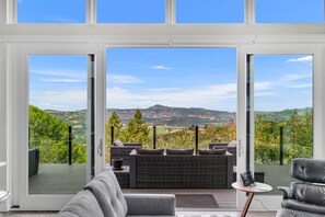 Un salon moderne doté d’une grande porte vitrée donnant sur une terrasse aménagée avec du mobilier d’extérieur.