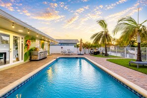 Ein Pool mit Fliesenbord, ein Grillplatz und eine Terrasse mit Gartenmöbeln.