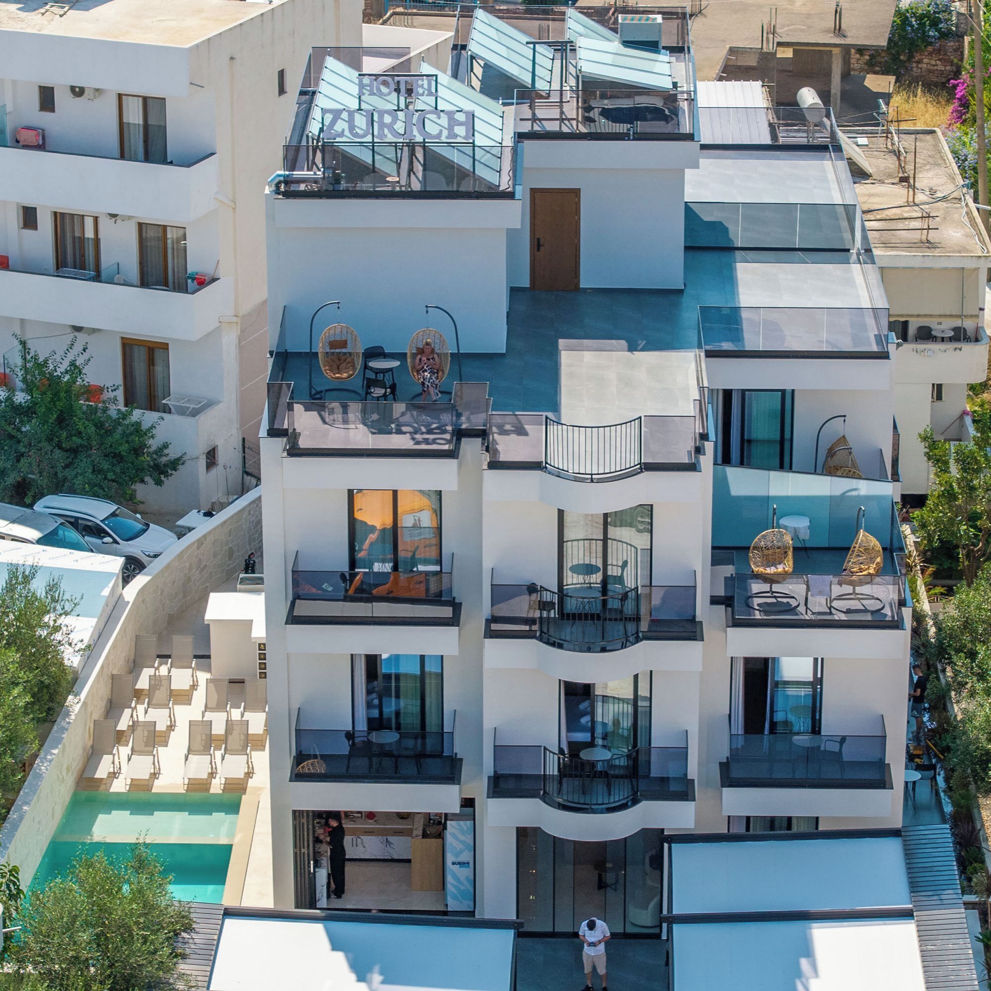A multi-story hotel with balconies, a swimming pool, and a rooftop terrace.