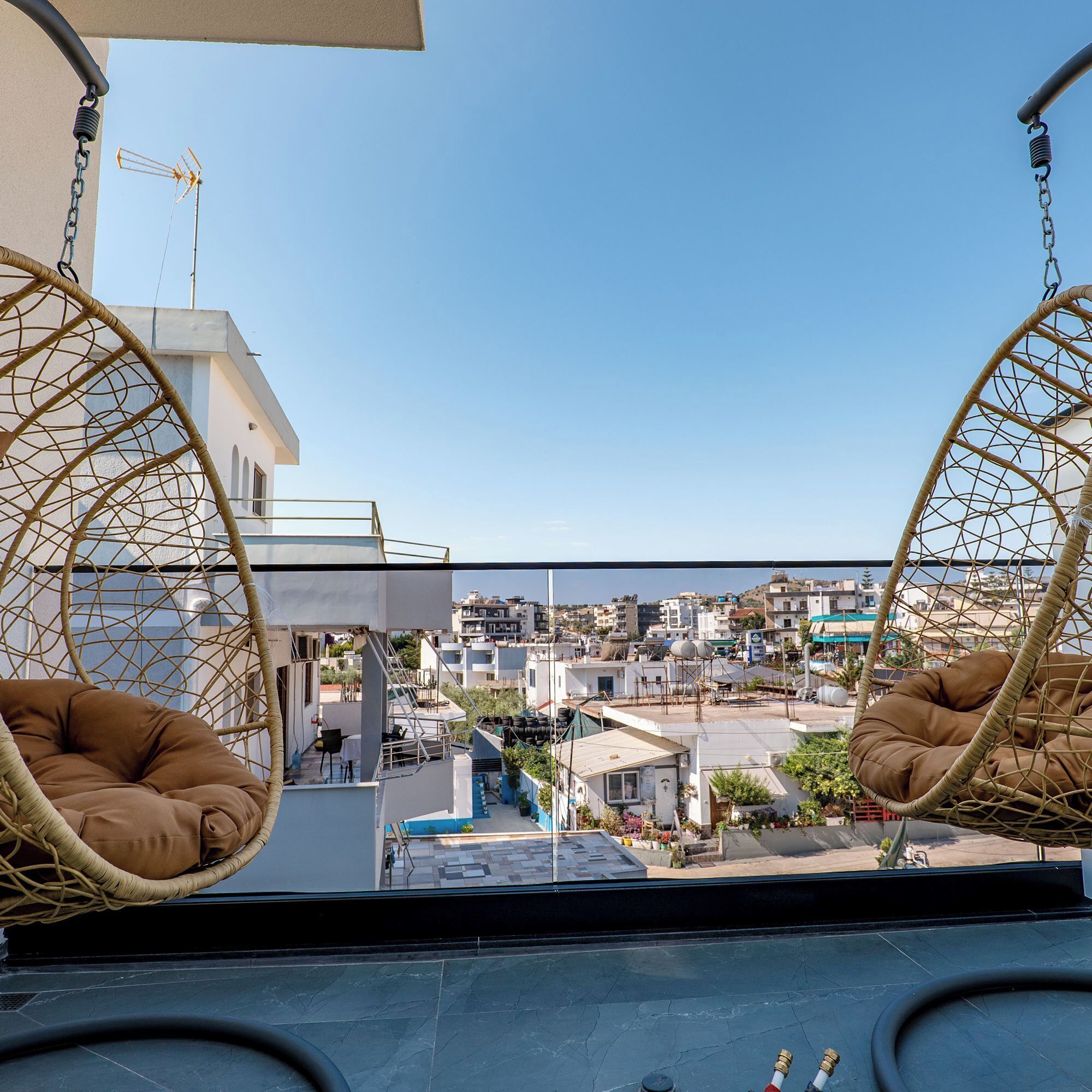 A balcony with two wicker swing chairs, a view of a cityscape, and a clear sky.