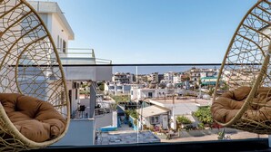 Un balcón con dos sillones colgantes de mimbre, vista a un paisaje urbano y cielo despejado.