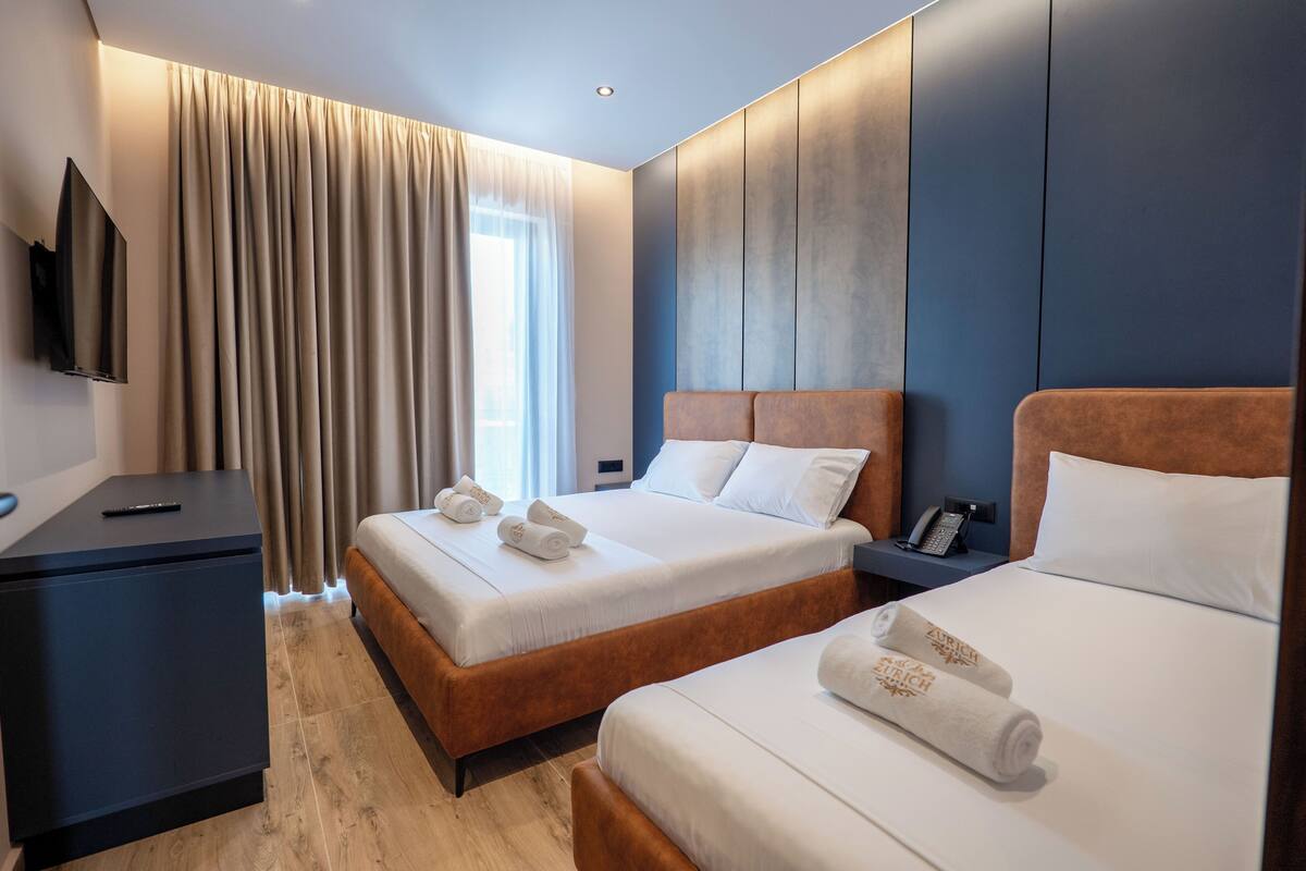 Habitació d'hotel amb dos llits, televisió, escriptori i finestra amb cortines.