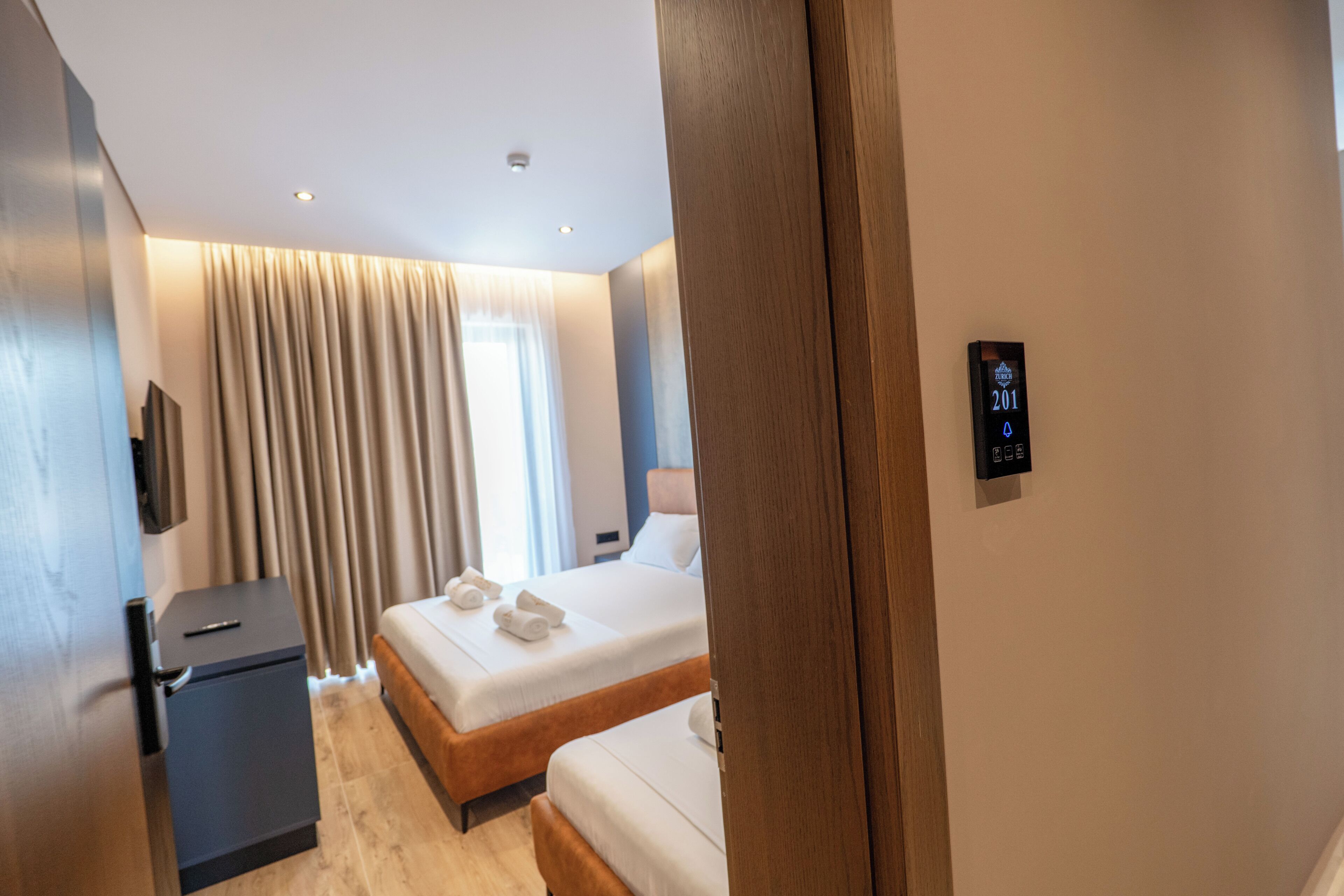 A hotel room with two beds, a minibar, a TV, and a digital thermostat.