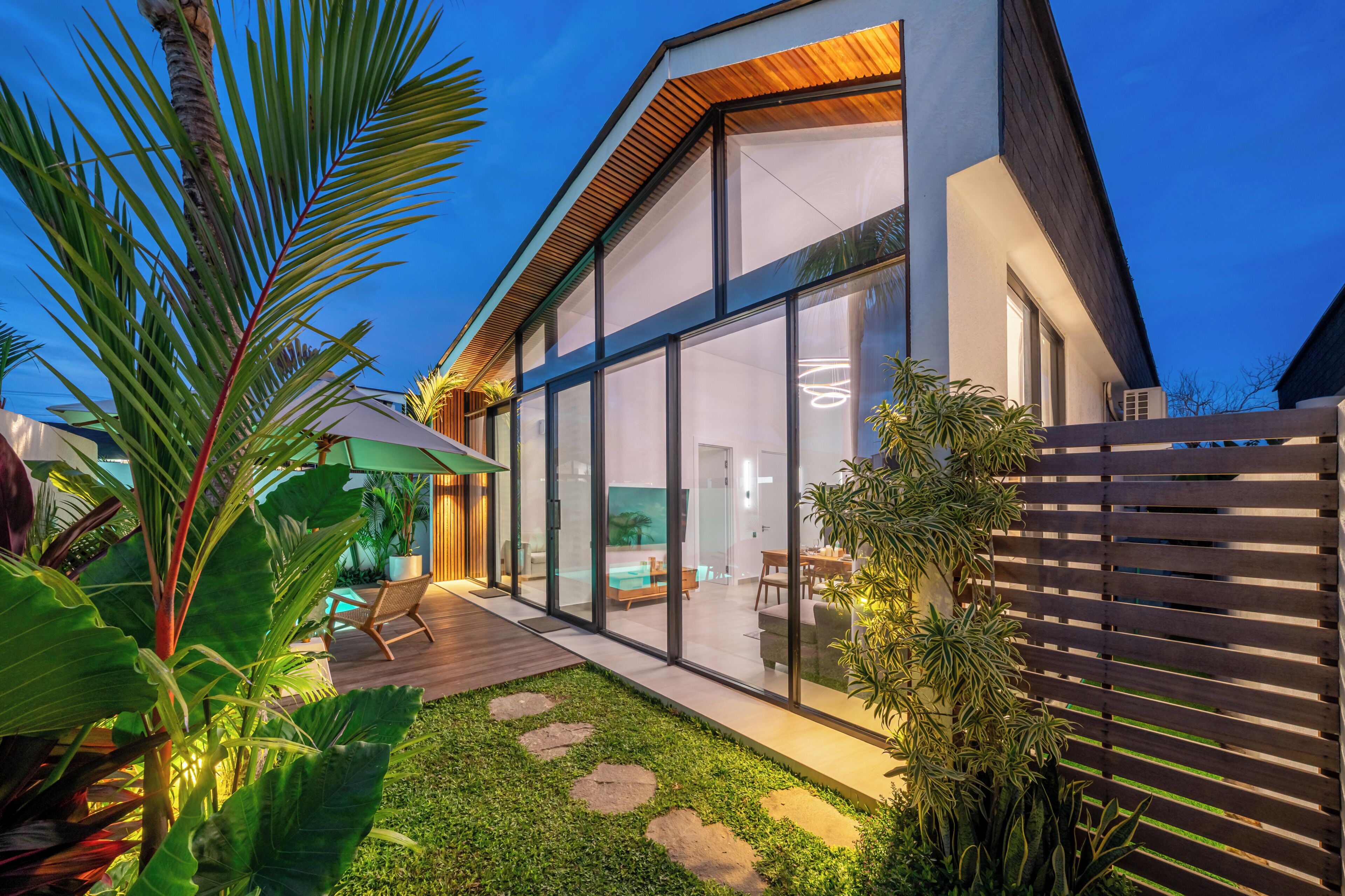 Een modern huis met grote glasramen, een houten terras en een verzorgde tuin.