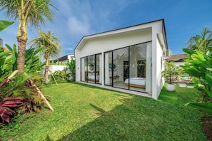 A modern house with a glass-enclosed bedroom, a well-maintained lawn, and tropical plants. - Oasis Pandawa (Kutuh)