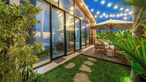 Een modern huis met grote glasramen, een houten terras en tuinmeubilair.