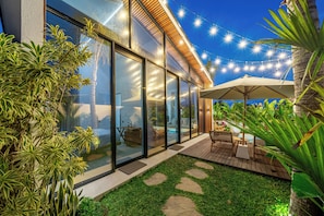 Une maison moderne dotĂ©e de grandes baies vitrĂ©es, dâune terrasse en bois et de mobilier dâextĂ©rieur.