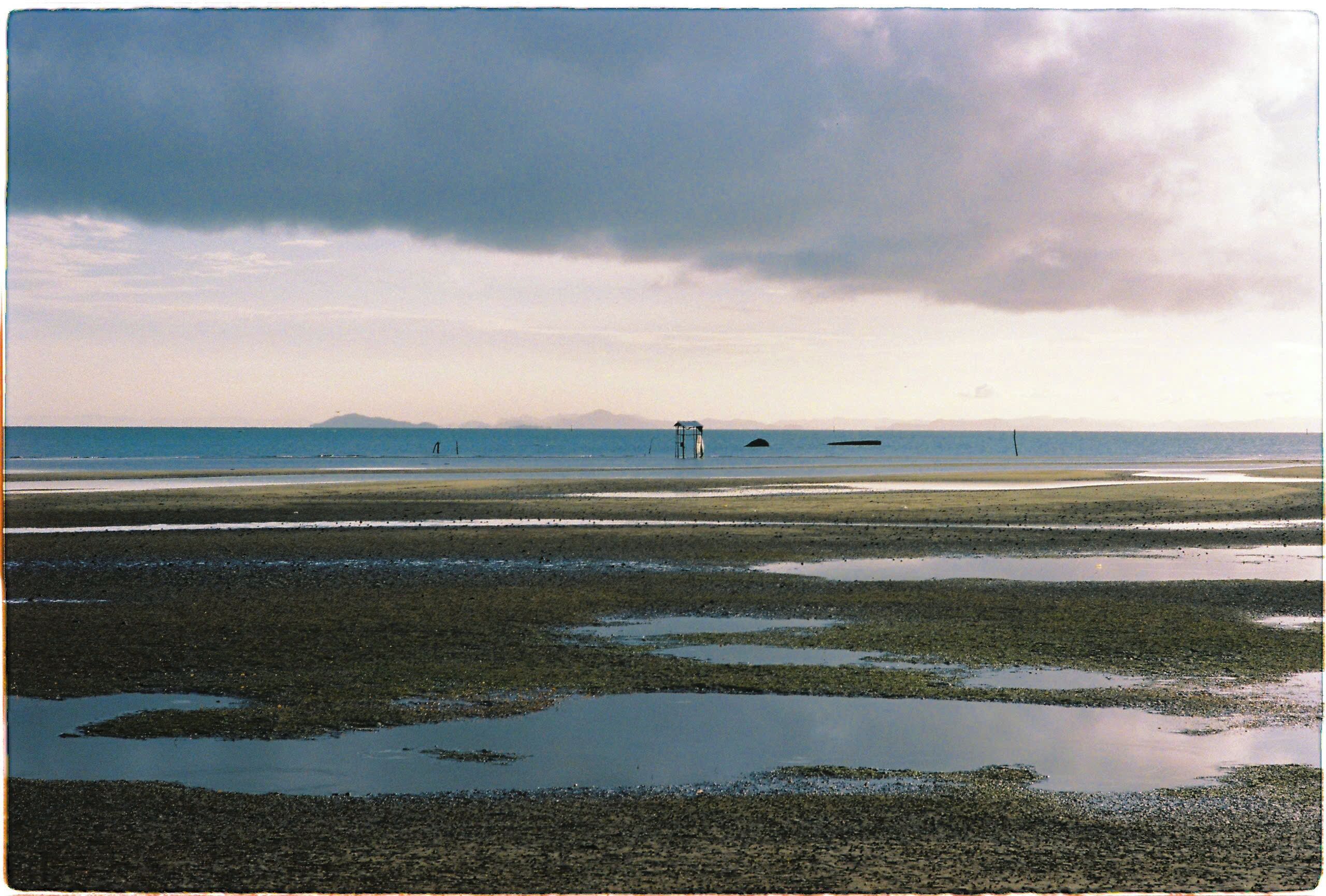 A coastal landscape with a beach, water, and distant mountains.
