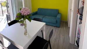 Ein Essbereich mit einem weißen Tisch, schwarzen Stühlen, einem türkisblauen Sofa und einer Vase mit Blumen.