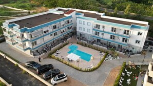 Un hotel de varios pisos con piscina en la azotea, mobiliario exterior y zona de estacionamiento.