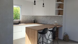 Eine moderne Küche mit einer Holztheke, zwei schwarzen Barhocker und Pendelleuchten.
