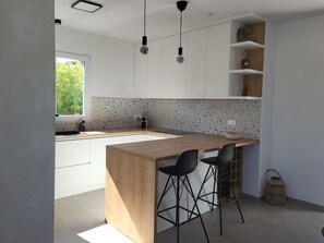 Eine moderne Küche mit einer Holztheke, zwei schwarzen Barhocker und Pendelleuchten.