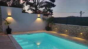 Ein Swimmingpool mit einer weißen Wand und einer Steinwand, umgeben von Topfpflanzen und Wandleuchten.