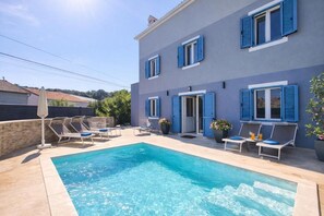 Un bâtiment à deux étages doté d’une piscine, d’un espace extérieur aménagé et de volets.