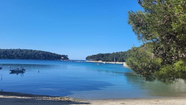 Ein Strand mit ruhigem Wasser, Booten und wolkenlosem Himmel.