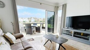 A living room with a sofa, a coffee table, a TV, and a balcony with a view of the city. - Beach Apartment in Amarilla Golf- Sleeps 4 (San Miguel de Abona)
