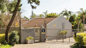 A gated entrance to Villa Elite with a paved driveway and a sign indicating the address. - Rosario’s Village | 2-Bed Unit 09, Bryanston (Bryanston)