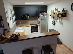 Eine kompakte Küche mit Kühlschrank, Mikrowelle, Backofen und einer kleinen Kochinsel mit Sitzgelegenheiten.