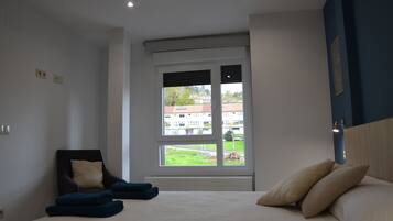 Un dormitorio con cama, una silla y ventana con vistas a edificios y follaje.