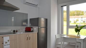 Una cocina moderna con un refrigerador de acero inoxidable, un tostador y una ventana que ofrece vistas a un edificio y árboles.