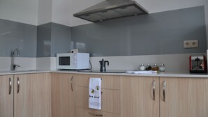 Moderni keittiö, jossa on mikroaaltouuni, vedenkeitin ja kaapistot.