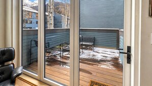 Una habitació amb una gran porta corredissa de vidre que dona a una terrassa exterior amb una banca i una cadira.