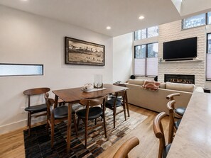 Ein modernes Wohnzimmer mit Esstisch, Stühlen, einer Couch, einem Kamin und einem an der Wand befestigten Fernseher.