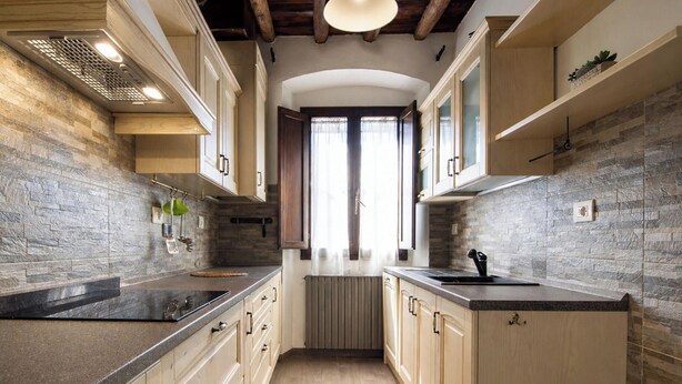 A narrow kitchen with wooden cabinets, a stone backsplash, and a central island. - Entire House Florence: 3 Bedrooms, 2 Bathrooms, and Free Parking by TuscanyWeGo (Firenze)