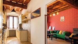 A kitchen with wooden cabinets and a stone backsplash, a dining area with a green sofa and a red brick wall, and a wooden ceiling. - Entire House Florence: 3 Bedrooms, 2 Bathrooms, and Free Parking by TuscanyWeGo (Firenze)