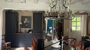 Een eetgedeelte met een grote tafel, stoelen, een kroonluchter en uitzicht op de keuken.
