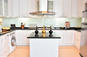 A modern kitchen with white cabinets, a central island, a stainless steel range hood, and a washing machine. - 1 Bed Serviced Skyvilla with view (Krung Thep Maha Nakhon)