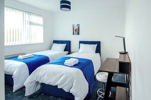 A hotel room with two beds, a desk, a chair, a lamp, and a window with blinds. - Spacious 5BR House, Sleeps 8-10, Fast Wi-Fi, Free Parking, Central Nottingham. (Nottingham)