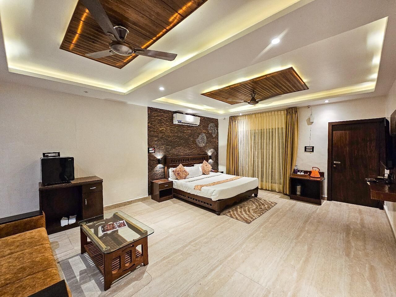 Ein modernes Hotelzimmer mit einem großen Bett, einem Schreibtisch, einem Fernseher und einem Deckenventilator.