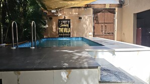 A swimming pool with metal railings, a sign reading 'Serenity The Villa,' and a door with a brown shutter. - Serenity the villa by Beta Bawarchi (Pachmarhi)