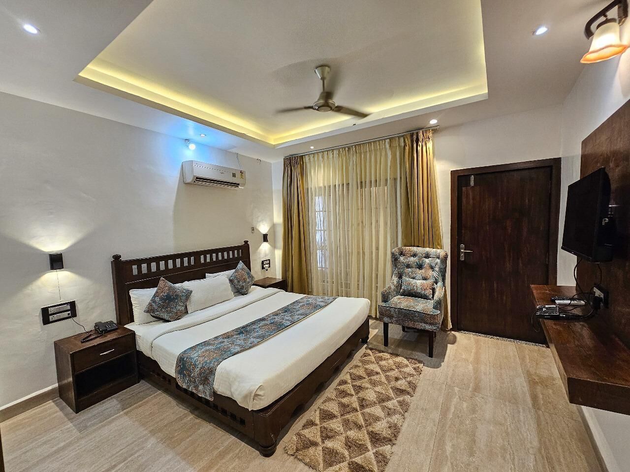 A modern bedroom with a bed, nightstand, chair, TV, and ceiling fan.