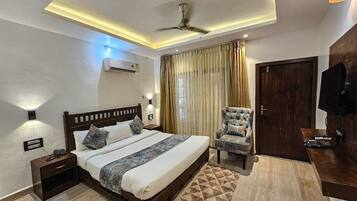 A modern bedroom with a bed, nightstand, chair, TV, and ceiling fan.