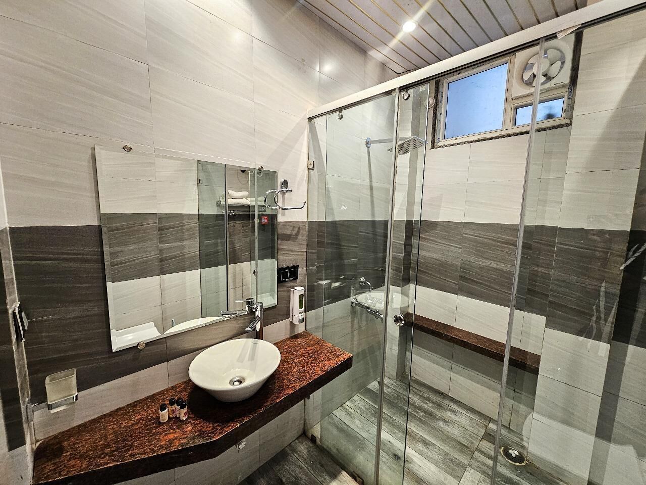 A modern bathroom with a glass shower enclosure, a sink with a marble countertop, and a large mirror.