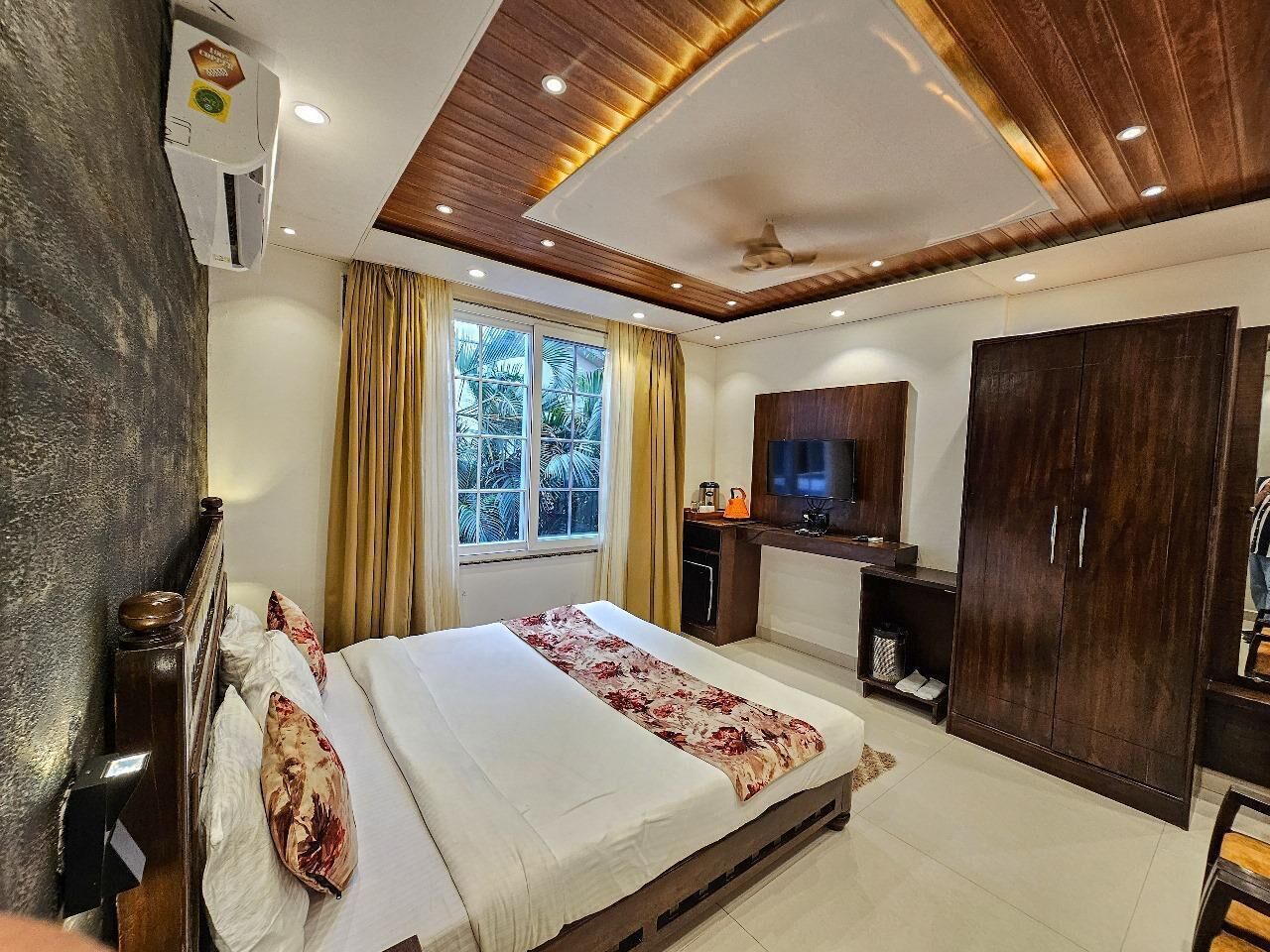 A bedroom with a bed, a wardrobe, a TV, and a window with curtains.