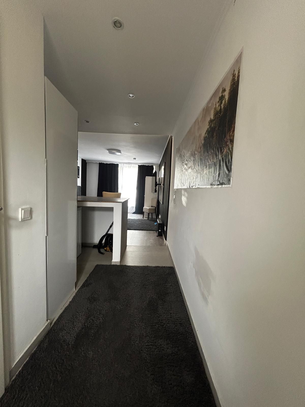 Ein Flur mit Teppichboden, einem Bild an der Wand und einer Tür, die in einen Raum mit einem Bett und einem Sessel führt.
