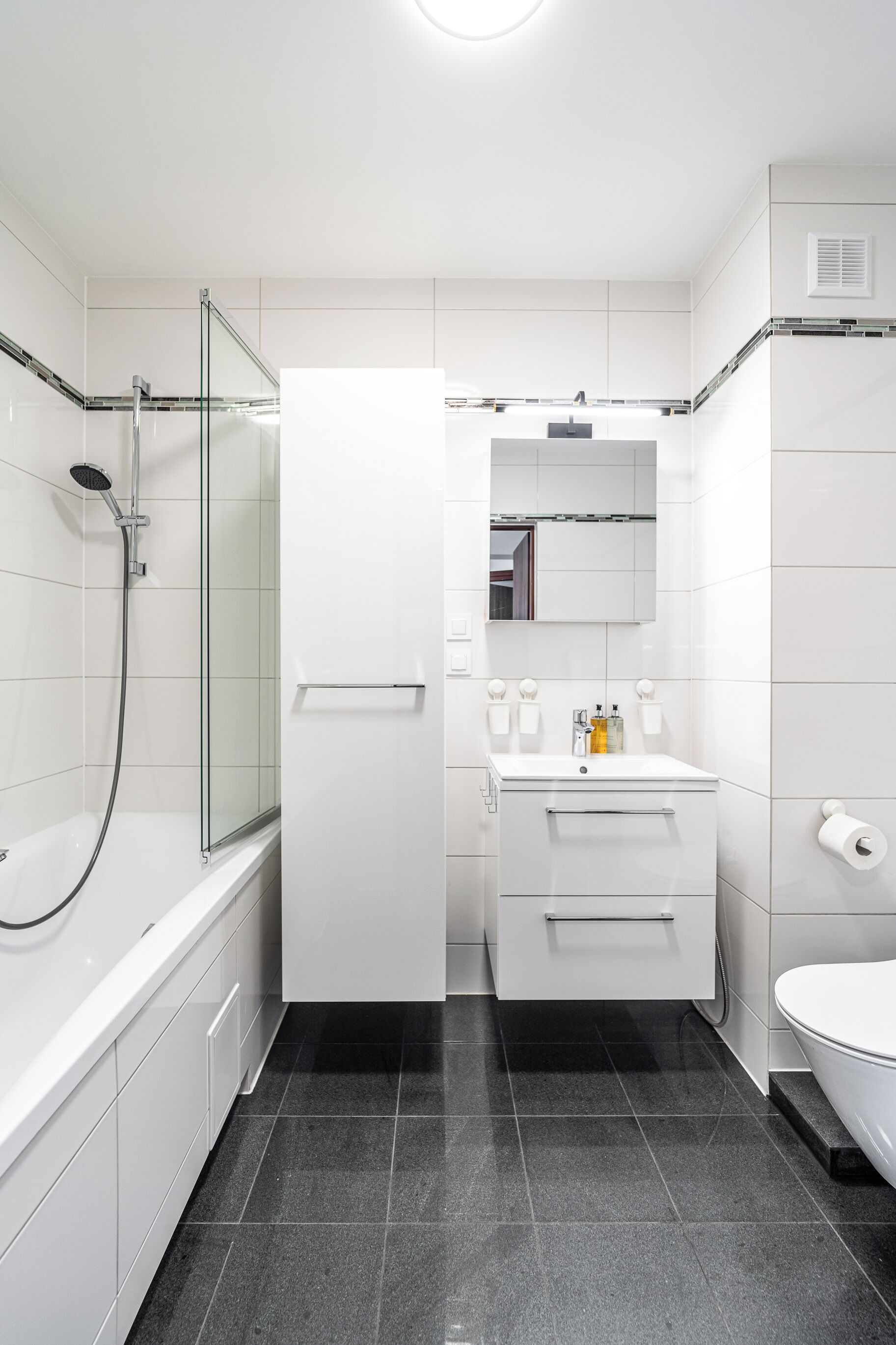 Ein modernes Badezimmer mit einer gläsernen Duschkabine, einem weißen Waschtisch mit Spiegel und einer Toilette.