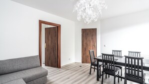 Un salón moderno con un sofá gris, una mesa de comedor de madera con sillas y una lámpara de techo blanca.